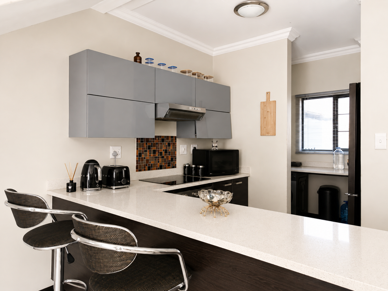 Modern kitchen featuring sleek grey cabinetry, quartz countertops, a breakfast bar, and a mosaic tile backsplash, with an adjacent scullery area.