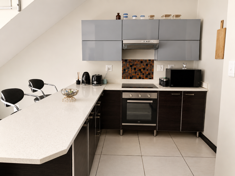 Modern kitchen featuring dark lower cabinets, grey upper cabinets, quartz countertops, built-in oven, electric hob, and a mosaic tile backsplash.