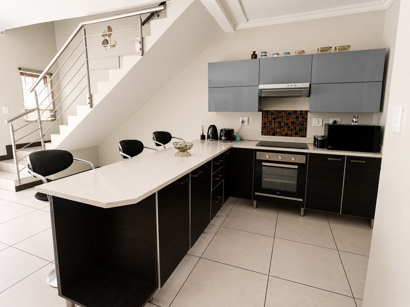 Modern kitchen featuring dark wood cabinetry, light stone countertops, integrated oven and hob, and an adjacent staircase with stainless steel railing.