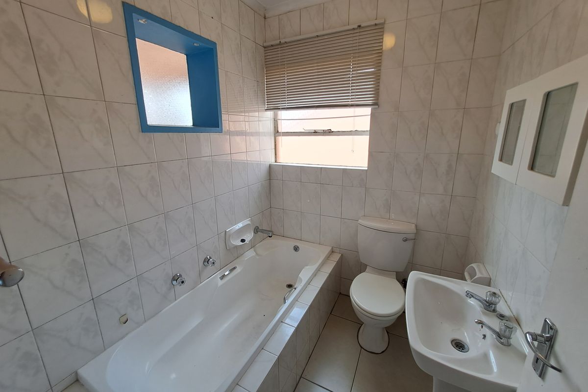 A functional bathroom featuring a built-in bathtub, pedestal basin, and toilet, finished with neutral wall tiles and a window for natural light.