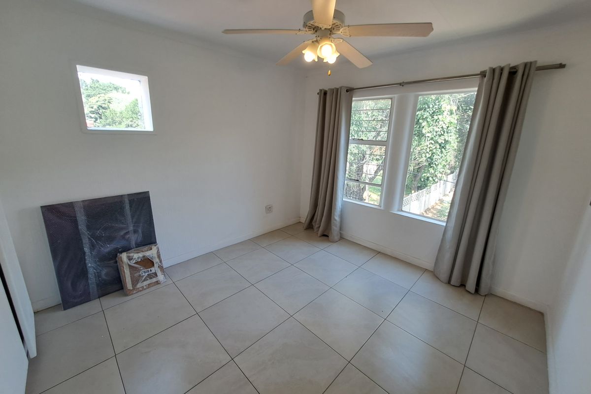 A bright, empty bedroom featuring neutral floor tiles, a ceiling fan, and large windows that provide ample natural light.