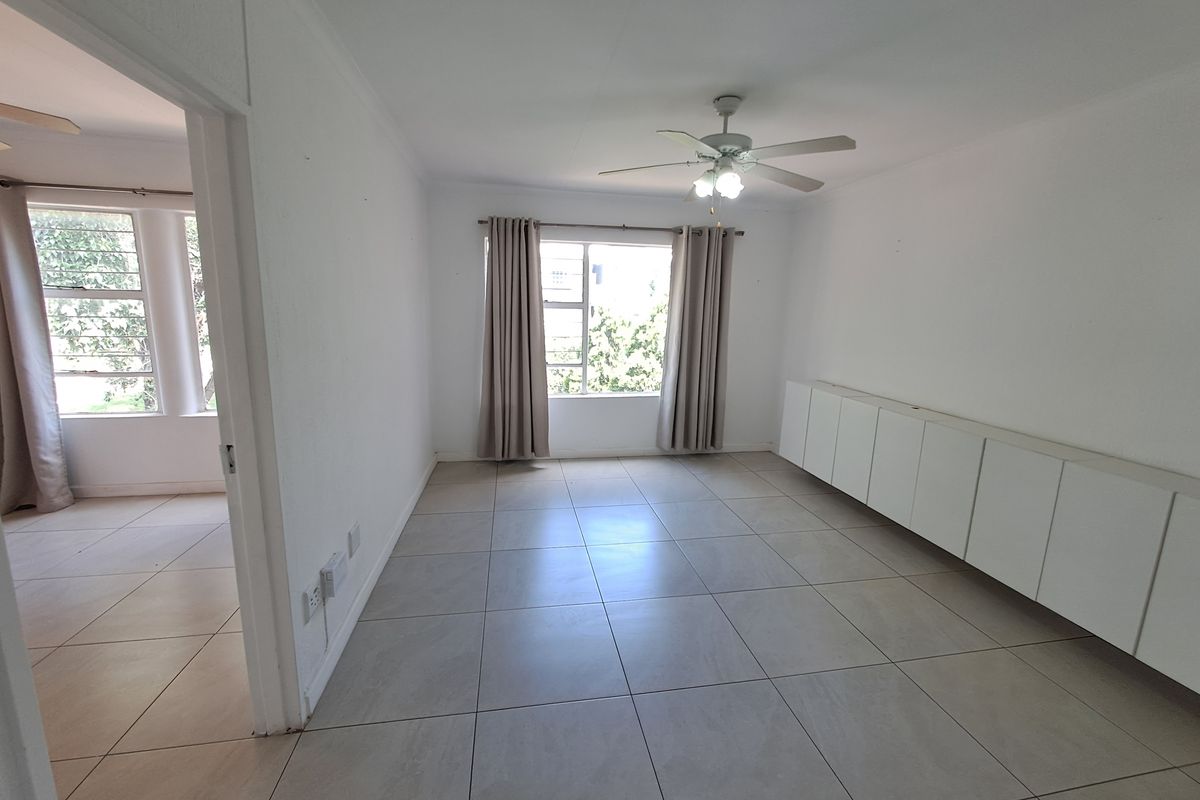 A bright, empty living room featuring large format floor tiles, a ceiling fan, and built-in storage cabinetry along the wall.
