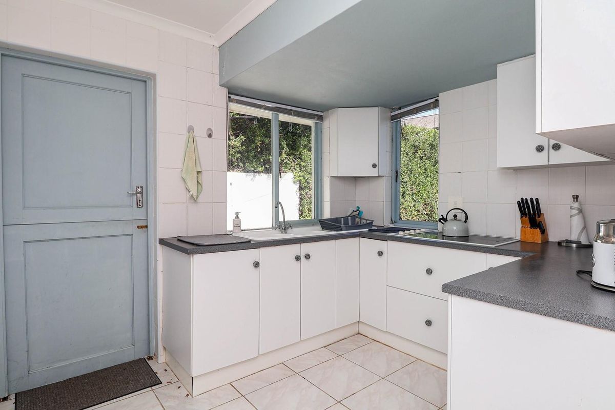 A functional kitchen featuring white cabinetry, dark laminate countertops, ceramic tile flooring, and a built-in electric hob with an integrated extractor fan.