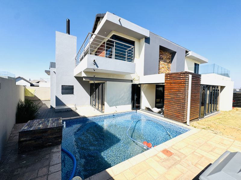 Modern double-story residence featuring a swimming pool, paved patio area, timber accents, and an upper-level balcony with stainless steel railings.