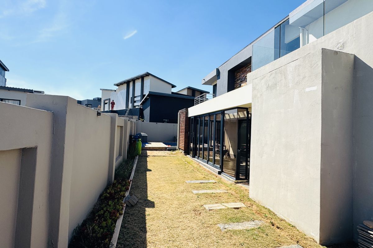 Rear exterior view of a modern home featuring a glass-enclosed living area, stone accents, and a private garden space with a paved walkway.