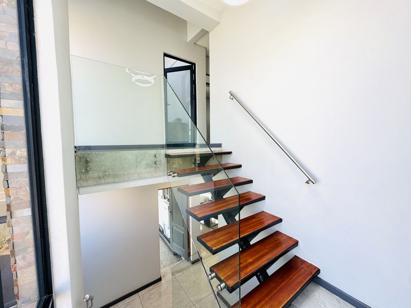 Modern entry area featuring a striking floating staircase with timber treads, glass balustrades, and a sleek stainless steel handrail.