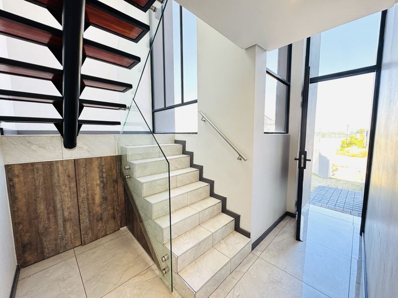 Modern entrance foyer featuring a striking floating staircase with glass balustrades, tiled flooring, and built-in storage cabinetry under the stairs.