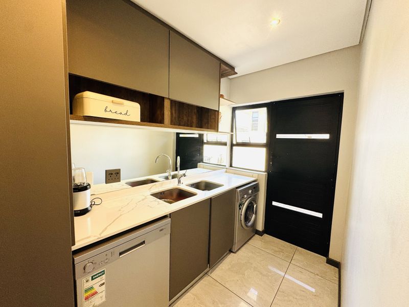 Modern scullery featuring sleek cabinetry, stone countertops, integrated sink, and tiled flooring, providing a functional and stylish secondary kitchen or utility space.