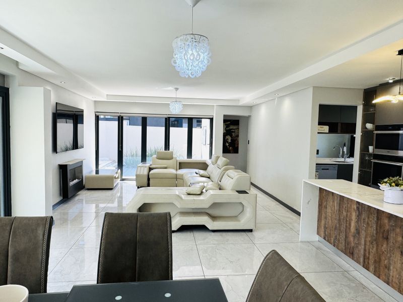Modern open-plan living area featuring large porcelain tiles, a sleek kitchen island, built-in fireplace, and seamless flow to the outdoor patio through sliding doors.