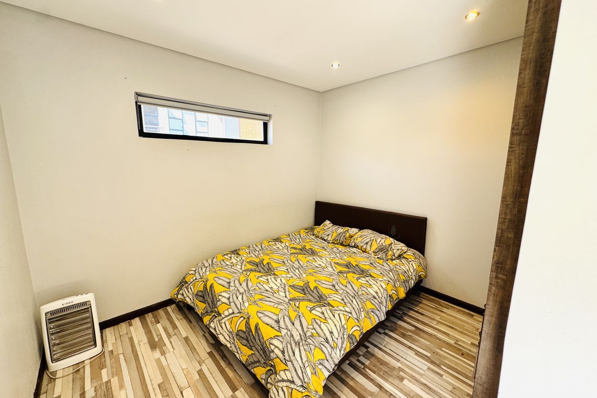 A compact bedroom featuring modern laminate flooring, recessed downlighting, and a horizontal clerestory window for natural light.