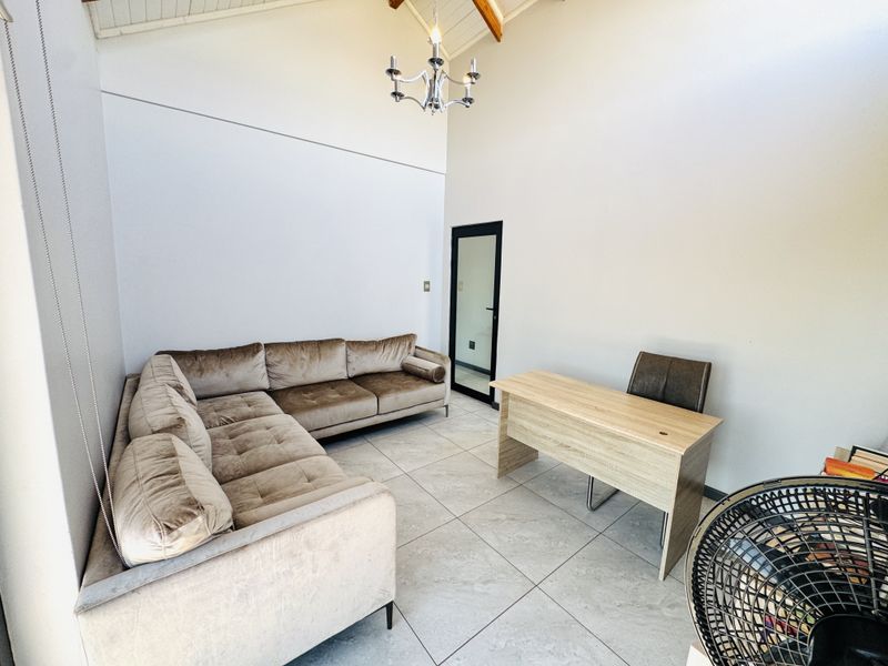 Spacious living area featuring high vaulted ceilings with exposed timber rafters, tiled flooring, and a modern chandelier, creating an open and airy atmosphere.