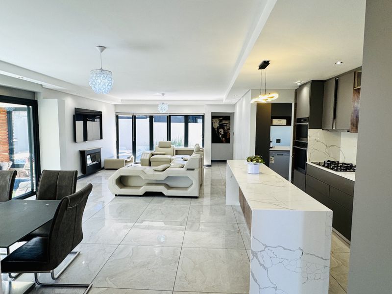 Modern open-plan living area featuring a sleek kitchen with quartz island, built-in appliances, and seamless flow to the outdoor patio through sliding glass doors.