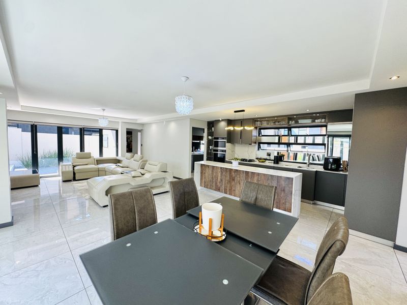 Spacious open-plan living, dining, and kitchen area featuring modern cabinetry, a central island, high-gloss tiled floors, and large sliding doors leading to the exterior.