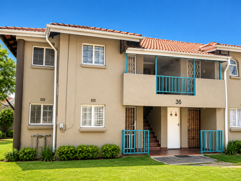 Front elevation of a two-story apartment building featuring a terracotta tiled roof, stucco exterior, and balcony with security railings.
