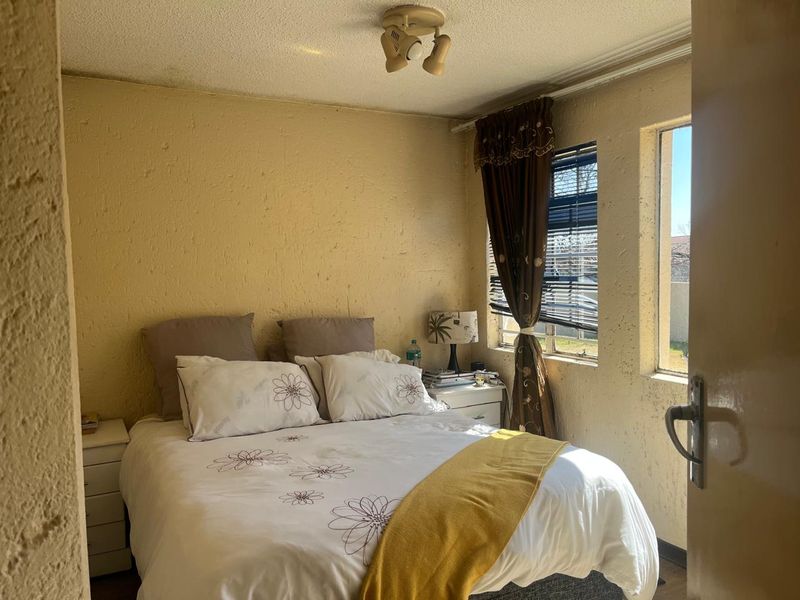 A compact bedroom featuring textured walls, a ceiling-mounted spotlight fixture, and a window with blinds, offering a functional space with potential for cosmetic updates.