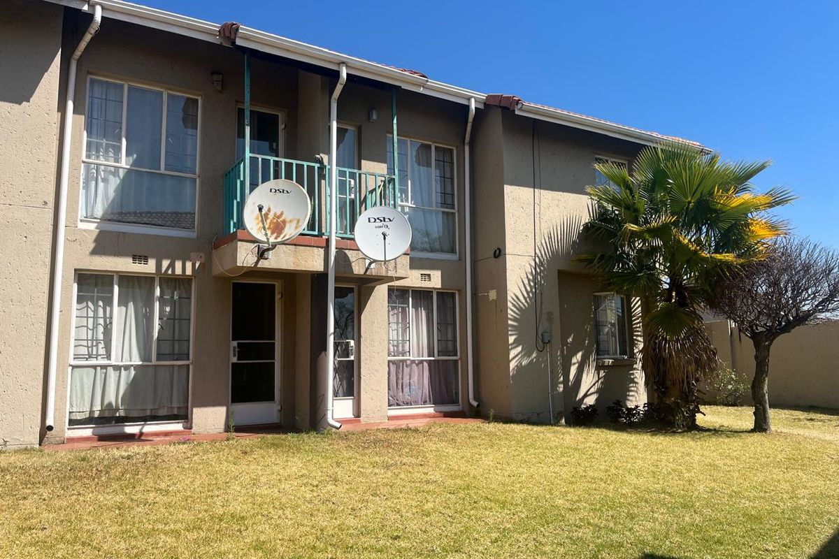 Rear view of a two-story apartment building featuring a balcony, sliding doors, and a small private garden area.