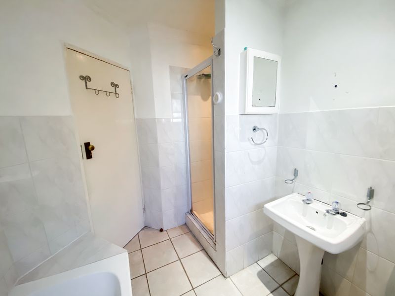 A functional bathroom featuring a pedestal basin, a separate shower enclosure, and neutral wall and floor tiling.