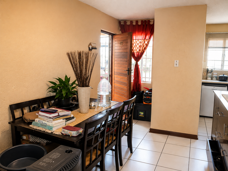 Open plan living and dining area featuring tiled flooring, a timber entrance door, and an adjacent kitchen space with built-in cabinetry.