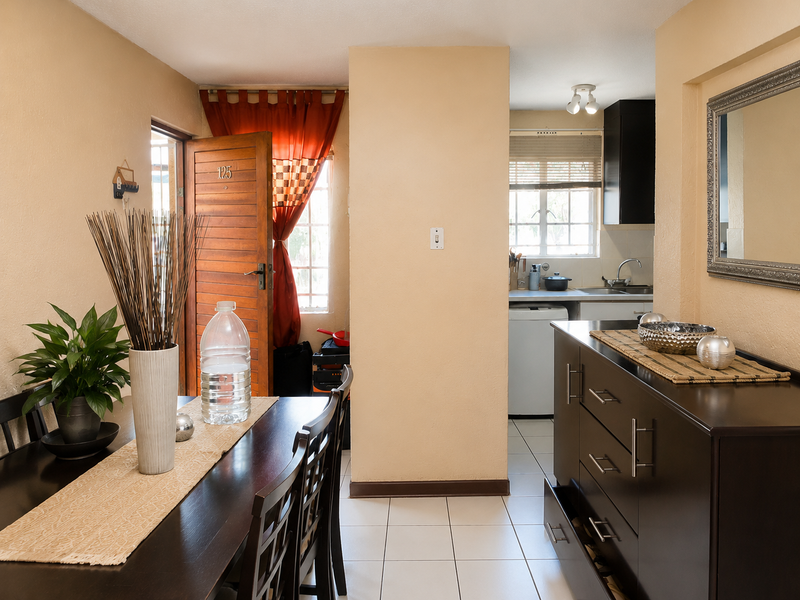 Open plan dining and kitchen area featuring tiled flooring, neutral wall tones, and direct access to the exterior through a timber entrance door.