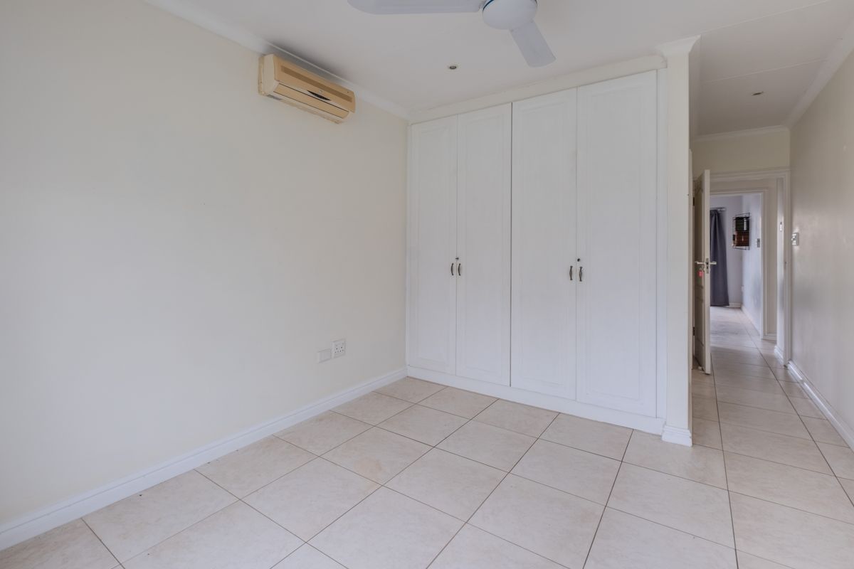 A bedroom featuring built-in white cabinetry, tiled flooring, and a wall-mounted air conditioning unit, leading into a hallway.