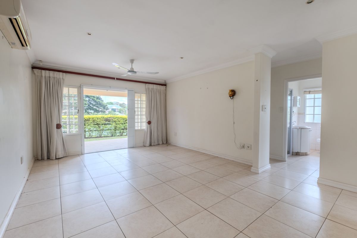 Spacious open-plan living area featuring neutral floor tiles, a ceiling fan, wall-mounted air conditioning unit, and sliding glass doors leading to a patio.