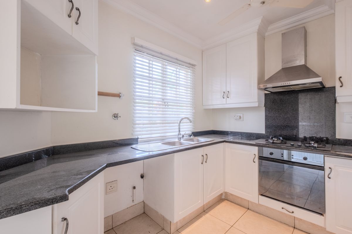 A functional kitchen featuring white cabinetry, dark granite countertops, a built-in oven, gas hob, and stainless steel extractor fan.