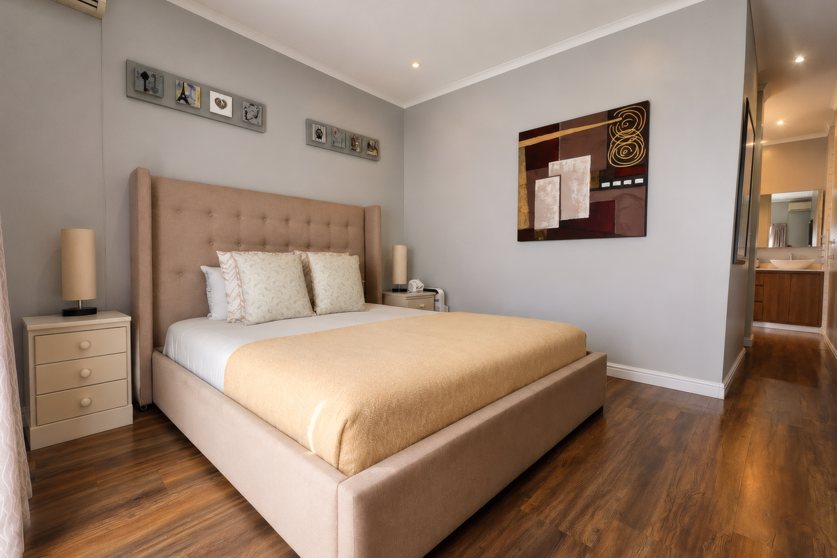 A well-maintained bedroom featuring laminate wood flooring, recessed downlighting, and a wall-mounted air conditioning unit, with direct access to an en-suite bathroom.