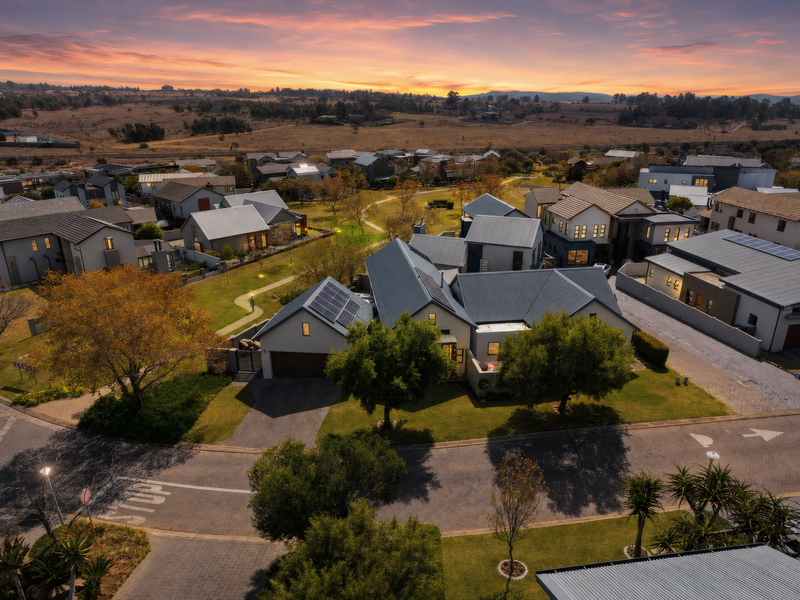 Aerial view of a modern residential estate featuring homes with metal roofs, solar panels, and well-maintained landscaped gardens at sunset.