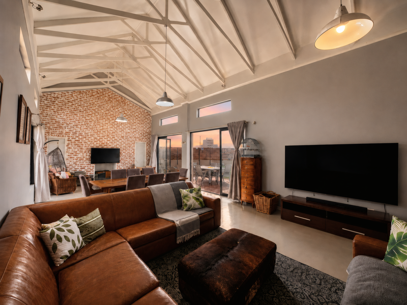 Spacious open-plan living and dining area featuring a striking exposed brick wall, vaulted ceilings with exposed trusses, and seamless access to an outdoor patio.