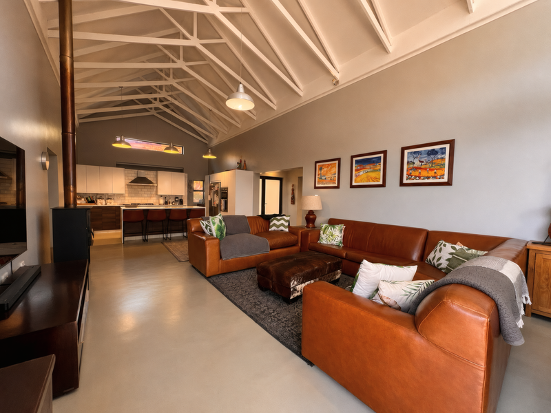 Spacious open-plan living area featuring a high vaulted ceiling with exposed rafters, a modern kitchen with island, and a cozy wood-burning stove.