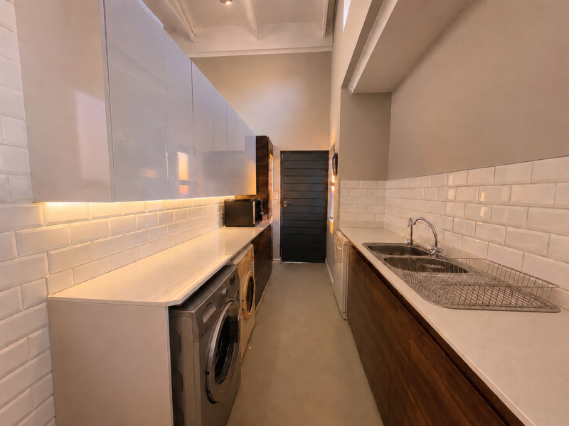 A modern, well-lit laundry room featuring sleek built-in cabinetry, stone countertops, subway tile backsplash, and integrated plumbing for laundry appliances.