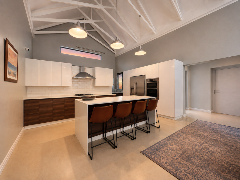 Modern kitchen featuring a high vaulted ceiling with exposed trusses, a central island, sleek cabinetry, and high-end built-in appliances.