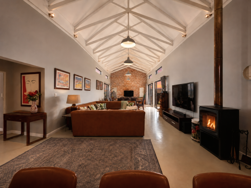 Spacious open-plan living area featuring a dramatic vaulted ceiling with exposed trusses, a striking brick feature wall, and a cozy wood-burning fireplace.
