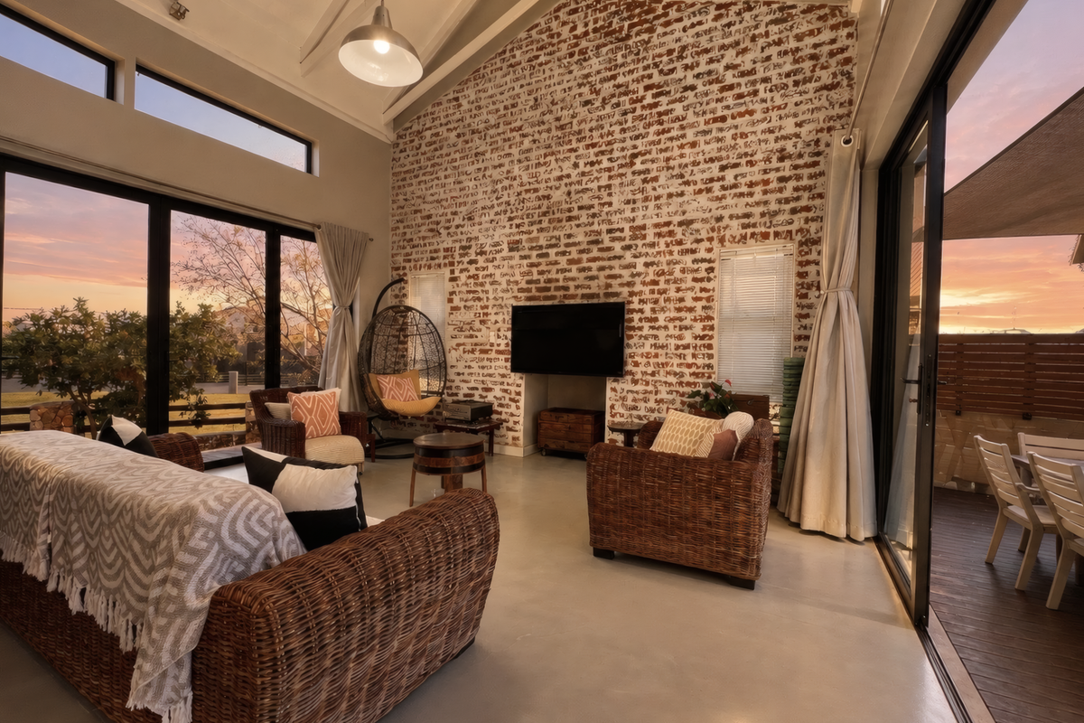 Spacious living room featuring a striking exposed brick wall, vaulted ceilings, polished concrete floors, and large sliding glass doors opening to an outdoor area.