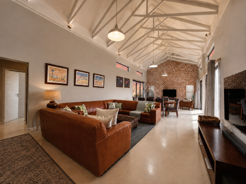 Spacious open-plan living and dining area featuring high vaulted ceilings with exposed trusses, polished concrete floors, and a striking exposed brick feature wall.