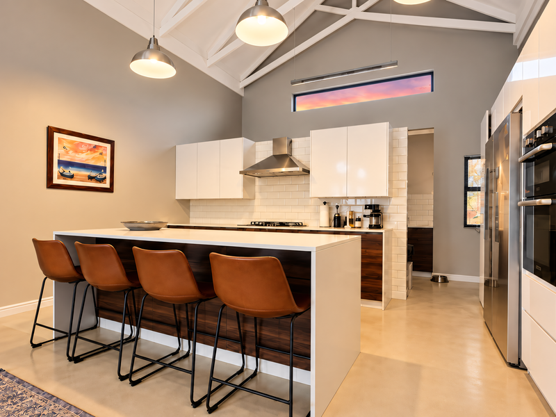 Modern kitchen featuring a large island, built-in appliances, subway tile backsplash, and vaulted ceilings with pendant lighting, set against polished concrete floors.