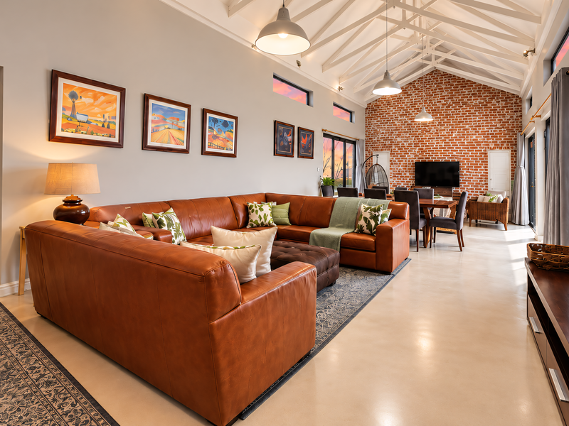 Spacious open-plan living and dining area featuring a vaulted ceiling with exposed trusses, a striking brick feature wall, and polished concrete floors.