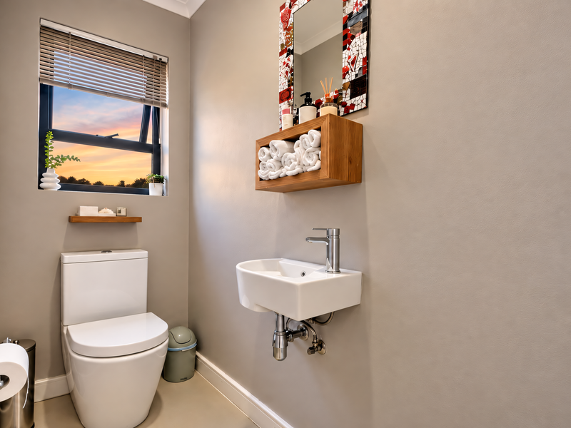 A modern, compact guest bathroom featuring a wall-mounted basin, chrome fixtures, and a toilet, finished with neutral tones and a window for natural light.