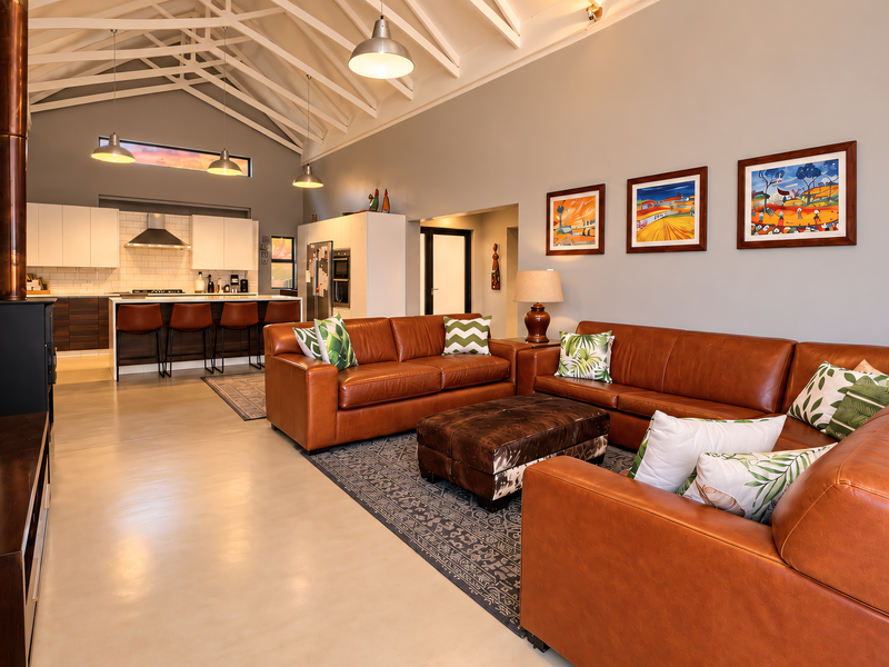 Spacious open-plan living area featuring a vaulted ceiling with exposed rafters, polished concrete floors, a modern kitchen, and a cozy wood-burning fireplace.