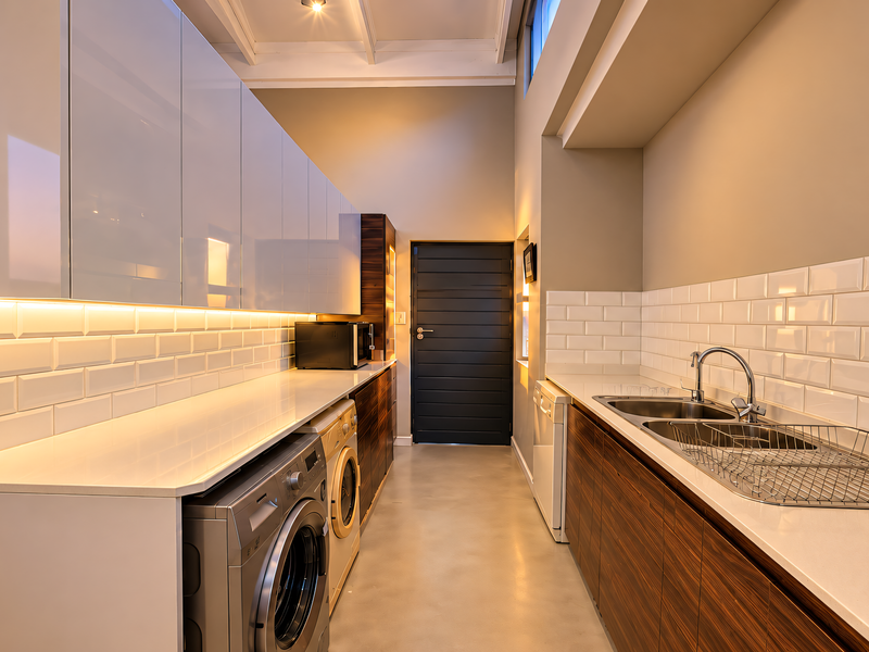 Modern, well-appointed laundry room featuring sleek cabinetry, stone countertops, subway tile backsplash, and a double stainless steel sink with integrated appliance space.