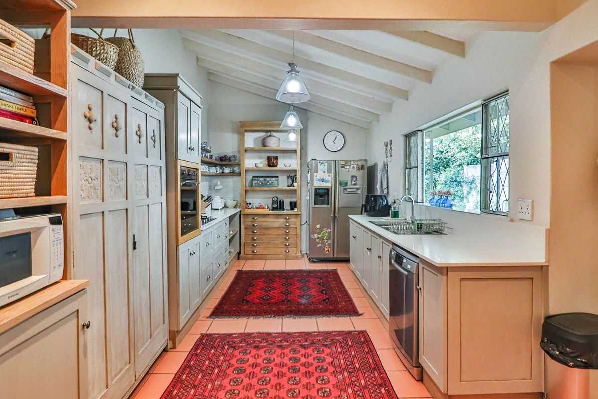 A spacious kitchen featuring light-toned cabinetry, stone countertops, exposed timber ceiling beams, and tiled flooring, offering a functional and character-filled cooking space.