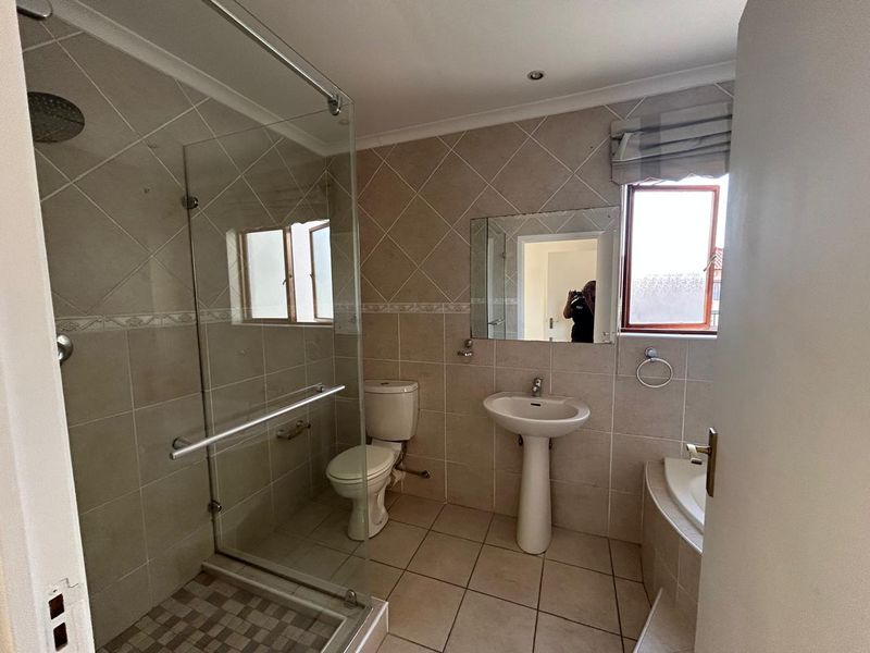 A functional bathroom featuring a glass-enclosed shower, pedestal basin, and a built-in bathtub with neutral wall and floor tiling.