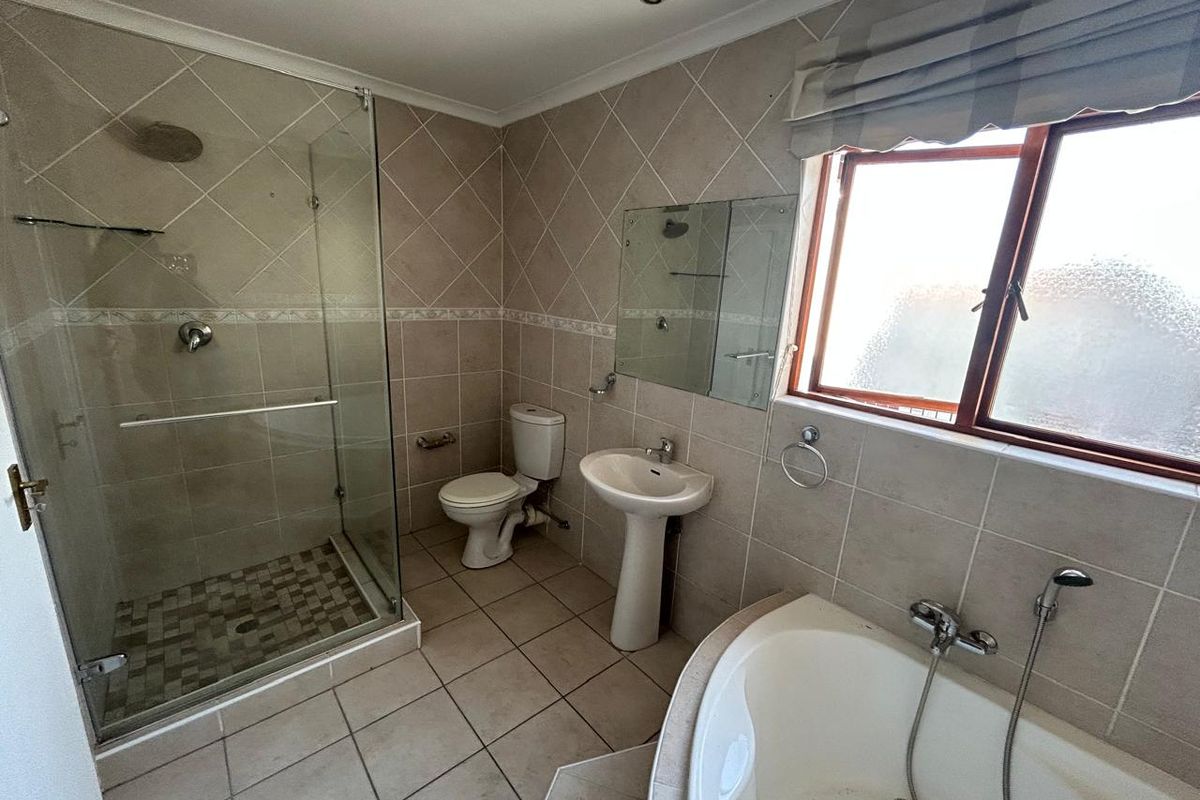 A functional bathroom featuring a glass-enclosed shower, corner bathtub, pedestal basin, and neutral tiled finishes throughout.