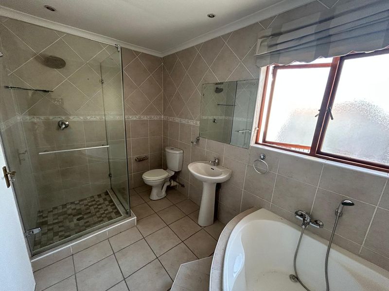 A functional bathroom featuring a glass-enclosed shower, corner bathtub, pedestal basin, and neutral tiled finishes throughout.
