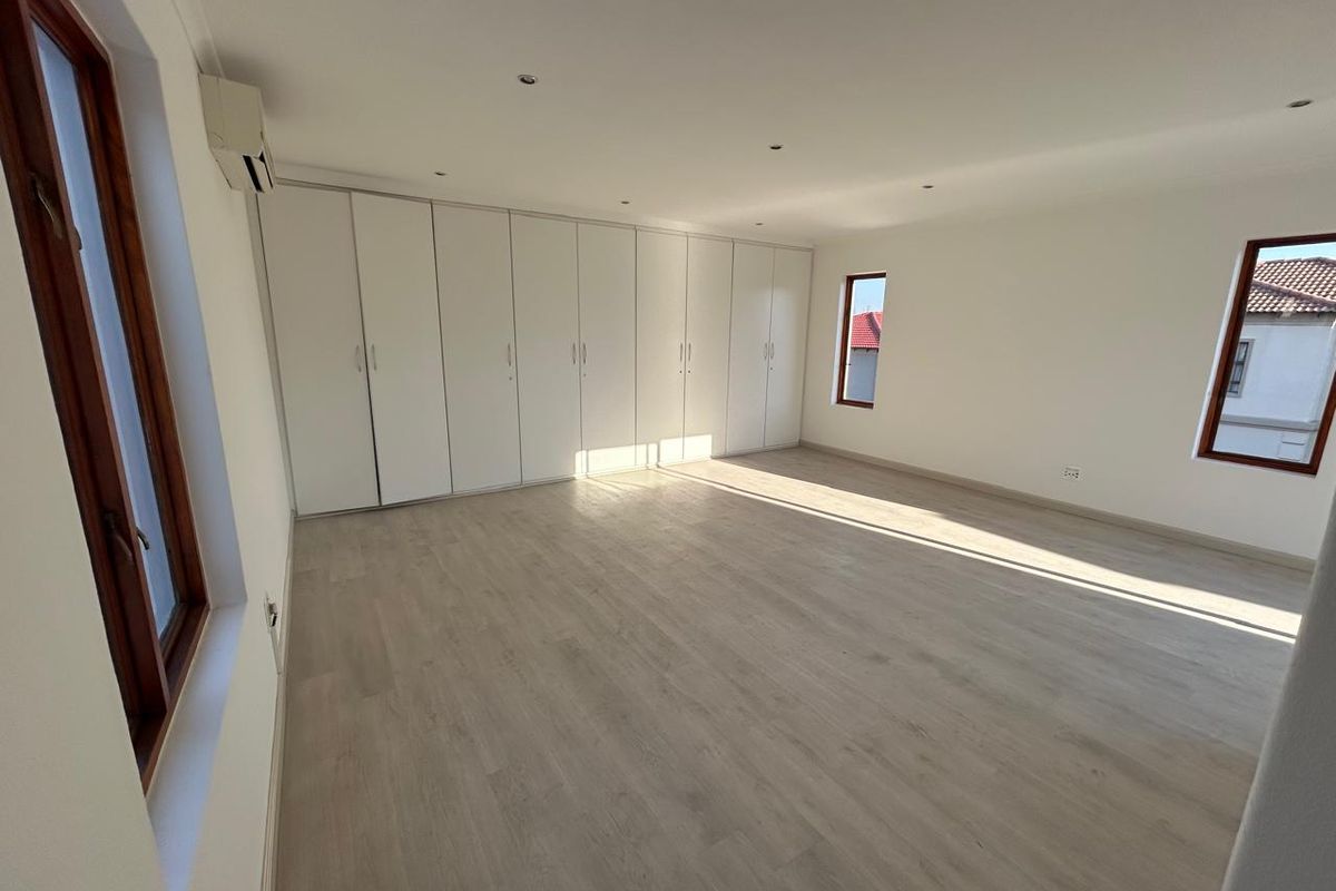 Spacious, light-filled bedroom featuring neutral laminate flooring, extensive built-in cabinetry, and an integrated air conditioning unit.
