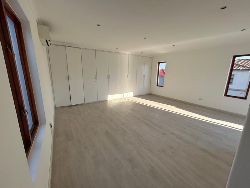 Spacious, light-filled bedroom featuring neutral laminate flooring, extensive built-in cabinetry, and an integrated air conditioning unit.