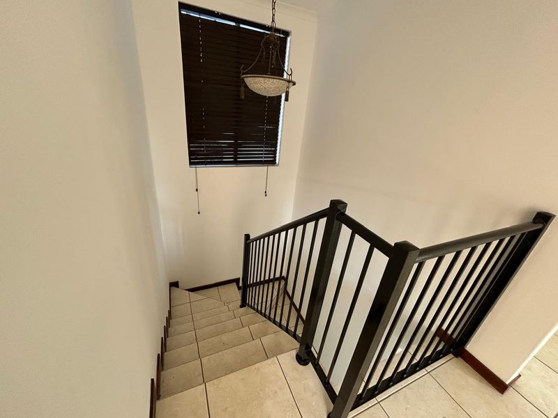 A bright staircase landing featuring tiled steps, a modern black metal balustrade, and a decorative pendant light fixture.