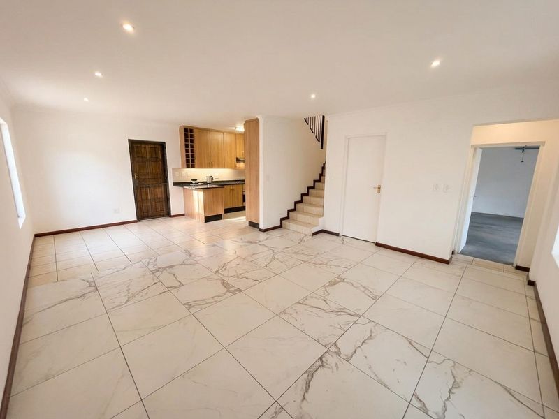 Spacious open-plan living area featuring large format marble-look floor tiles, recessed lighting, and a functional kitchen with built-in cabinetry and granite countertops.
