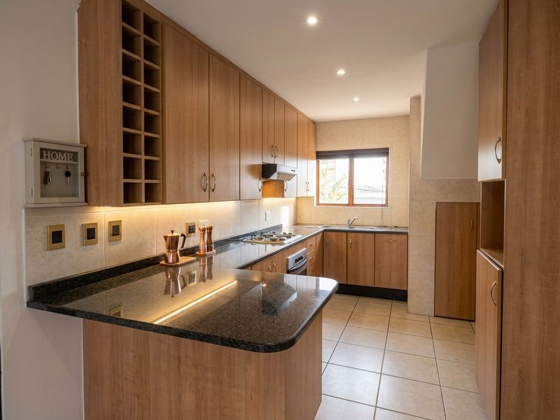A well-maintained kitchen featuring granite countertops, wooden cabinetry, integrated gas hob, oven, and extractor fan with modern under-cabinet lighting.