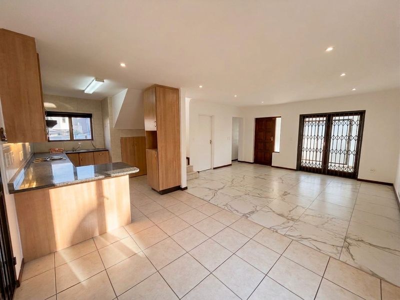 Spacious open-plan living and kitchen area featuring tiled flooring, granite countertops, ample built-in cabinetry, and direct access to the exterior via a security gate.